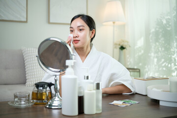 Asian woman in white robe preparing to cleanse her face with toner and cotton pad during her skincare routine.
