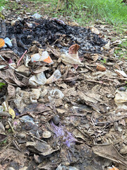 Charred fire pit with smoldering ashes and burnt leaf debris on dusty ground after garbage burning...