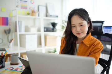 Young female graphic designer working on a creative project at her desk with color palettes and...
