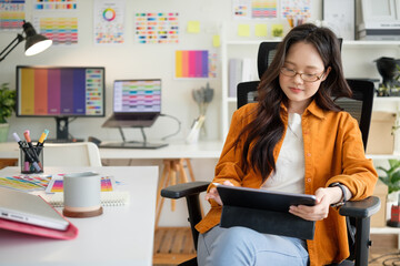 Young female graphic designer using a digital tablet while working in a  creative workspace.
