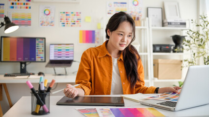 Female designer reviewing color palettes at her desk with a laptop and digital tablet. Bright,...