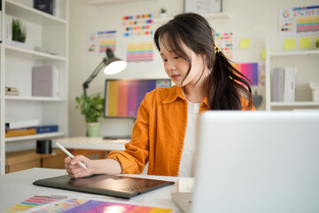 Young Asian woman working on a digital tablet with a stylus at a modern creative office. Focused...