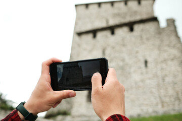 Hands of traveler photographing an ancient stone fortress with a smartphone in Vrsac, Serbia. Travel blogger making video outdoor