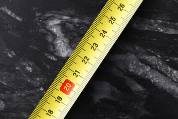 Yellow measuring tape on dark marble background. Close-up of metric ruler tool. Precision instrument for construction or tailoring. Bright color contrast on stone surface.