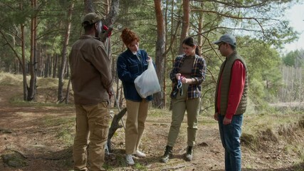 Red haired volunteer holding plastic bag with gardening gloves, she taking gloves and giving them to her companions before cleaning - Powered by Adobe