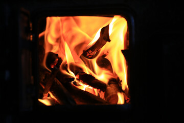 Close-up of intense flames and wood burning inside dark iron stove with visible inner firebox