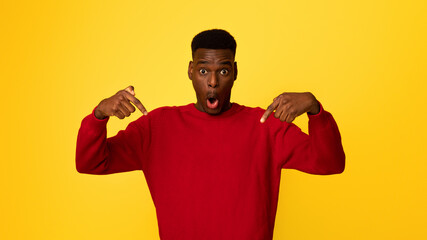 Shocked African American Guy Pointing Down With Fingers, Posing With Open Mouth Over Yellow Studio...
