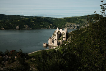 Elevated view of Golubac Fortress on the Danube, surrounded by lush green hills and blue sky. A popular tourist destination