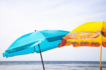 A blue and yellow beach umbrella stands on the sandy shore by the sea, offering shade under the...