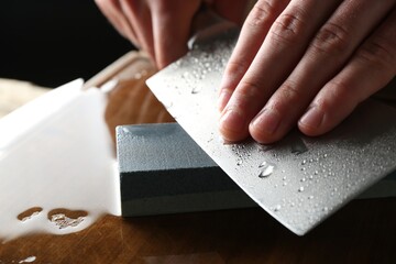 Man sharpening knife with sharpener on wooden table, closeup