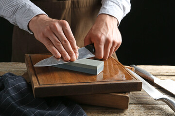 Man sharpening knife with sharpener on wooden table, closeup