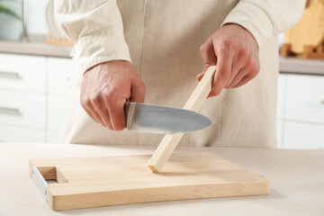 Man sharpening knife with sharpener at beige table indoors, closeup