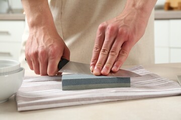 Man sharpening knife with sharpener at beige table indoors, closeup