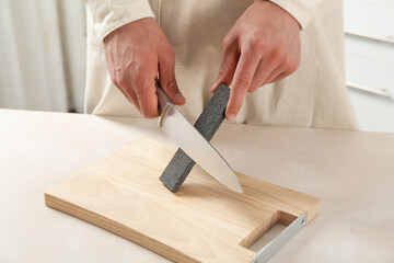 Man sharpening knife with sharpener at beige table indoors, closeup