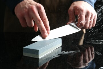 Man sharpening knife with sharpener at mirror table, closeup