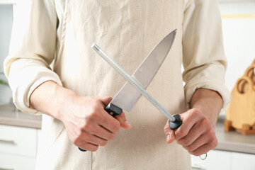 Man sharpening knife with sharpener indoors, closeup