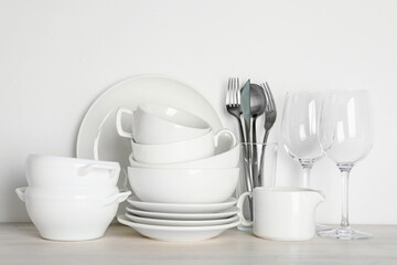 Different clean dishware on light wooden table near white wall