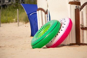 Two inflatable swim rings, one green and one pink, stand upright on a sandy beach near the sea,...