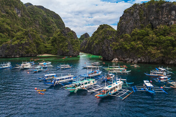 Tourists Kayaking Through the Turquoise Waters of Big Lagoon with impresive cliffs and bangka boats moored in a sunny day in Minoloc Island, El Nido, Palawan, Philippines