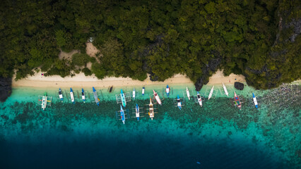 Top-Down bird's eye Aerial View of Bangka Boats Along the White Sand Shores of Entalula Island with a beautiful beach with people, El Nido, Palawan, Philippines