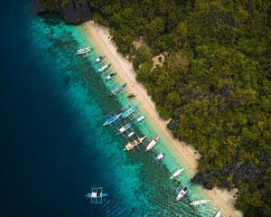 Top-Down bird's eye Aerial View of Bangka Boats Along the White Sand Shores of Entalula Island with a beautiful beach with people, El Nido, Palawan, Philippines
