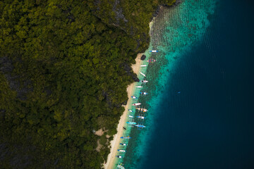 Top-Down bird's eye Aerial View of Bangka Boats Along the White Sand Shores of Entalula Island with a beautiful beach with people, El Nido, Palawan, Philippines