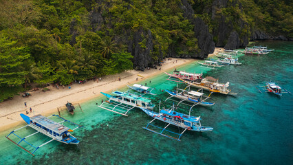 Aereal view of Colorful Bangka Boats Docked on the Crystal-Clear Waters and Coral Reefs of Entalula Island with a beautiful beach with people in El Nido, Palawan, Philippines