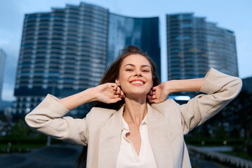 Confident smiling woman in beige blazer enjoying city skyscraper background, bright natural light,...