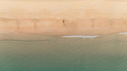 Bird's eye top aerial view of woman relaxing in sandy beach in the pristine turquoise shoreline and sweeping coastal landscape of Nacpan Beach in El Nido, Palawan, Philippines
