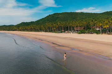 Bird's eye top aerial view of woman relaxing in sandy beach in the pristine turquoise shoreline and sweeping coastal landscape of Nacpan Beach in El Nido, Palawan, Philippines