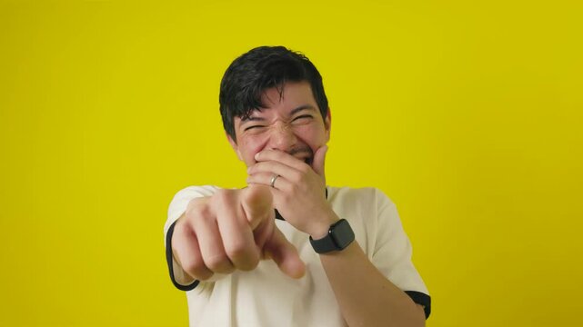Young freckled man with a cheerful mustache mockingly pointing with his hand on a yellow background with copyspace, concept of young man pointing in mockery