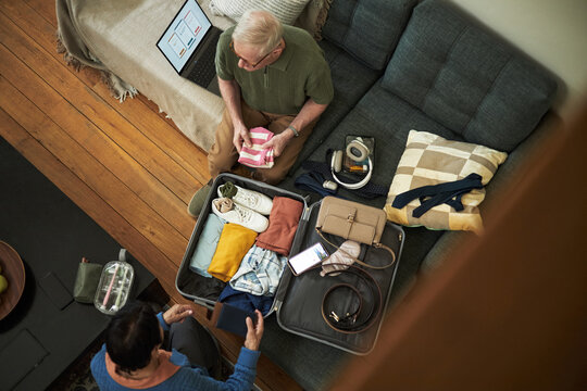 Overhead view of elderly couple diligently packing suitcase on couch with various items carefully arranged for an vacation trip abroad on holiday - Powered by Adobe