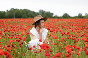 Young woman in a white dress and hat posing among summer poppies