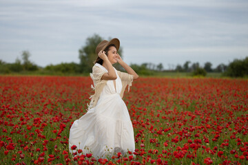 Young woman in a white dress and hat walks among summer poppies