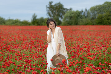 Young woman in a white dress and hat posing among summer poppies