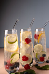 refreshing trio of tall glasses with citrus and berries in sparkling water, enhanced by elegant glass straws against a minimalist blue and beige setting. studio, closeup, decor, garnish, transparent