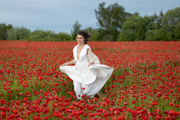 Happy young woman in a white dress runs through a summer poppy field