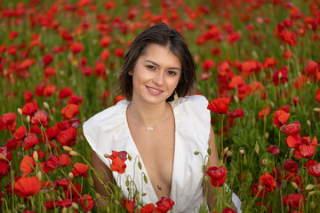 Young woman in a white dress posing among summer poppies