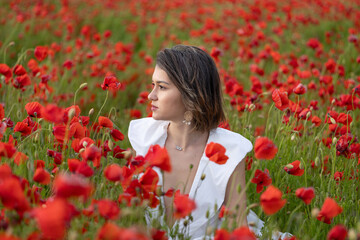 Young woman in a white dress posing among summer poppies