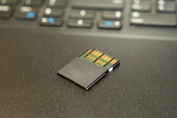 Close-up of a black SD memory card on a laptop keyboard background. Shallow depth of field and soft...