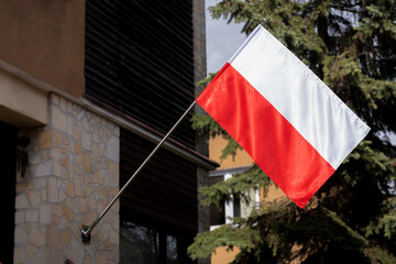 Polska flaga wisząca na uchwycie na domowej elewacji, flaga Polski zawieszona na zewnętrznej ścianie domu