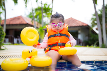 Cute little Asian girl wearing life jacket playing in swimming pool,Asian girl wearing life jacket...
