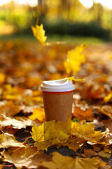 Eco zero waste paper cup take away with hot drink, coffee or tea outdoors in the sunny autumn park. Falling colorful leaves on background. Concept of seasonal warm drinks to go in cold weather.