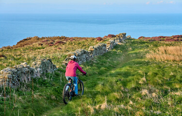 active senior woman riding her electric mountain bike at Mull of Galloway,  the southern most point...