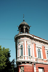 Historic red and white building with ornate tower and metal dome in Vrsac, Serbia, under clear blue sky.