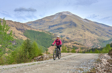 active senior woman riding her electric mountain bike in the Glen Nevis valley below Ben Nevis...