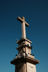 Stone cross monument with pigeons perched on it under a deep blue sky in Vrsac, Serbia. Religious symbol and historical landmark.