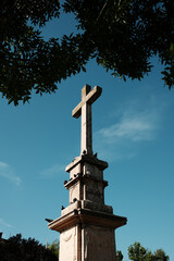 Stone cross monument with pigeons perched on it under a deep blue sky in Vrsac, Serbia. Religious symbol and historical landmark.