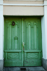 Old green wooden door with gothic arch shapes and a small wreath, located Vrsac town, Serbia.