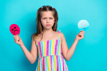 Smiling young girl holding happy and sad emotion signs in hands wearing colorful dress against...